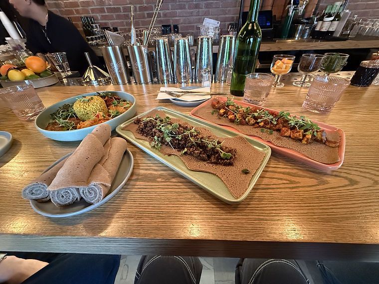 Shared platters of injera and stews at a restaurant counter